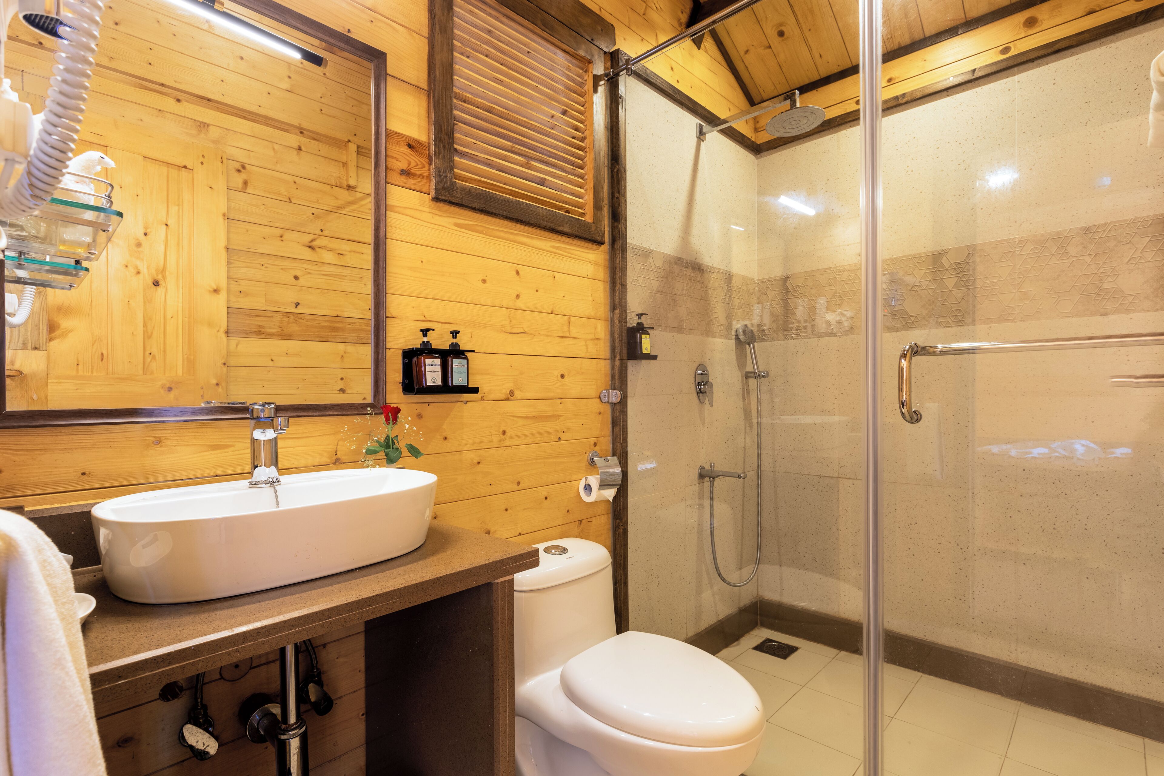 A bathroom with a wooden interior, a white sink, a toilet, and a glass-enclosed shower area.