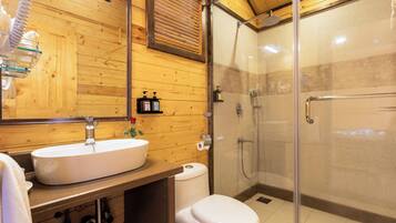 A bathroom with a wooden interior, a white sink, a toilet, and a glass-enclosed shower area.