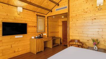 A wooden cabin interior with a bed, a desk, a chair, a TV, and a wall-mounted lamp.