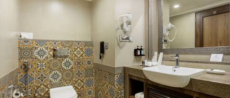 A bathroom with a white sink, a toilet, and a shower with a hairdryer.