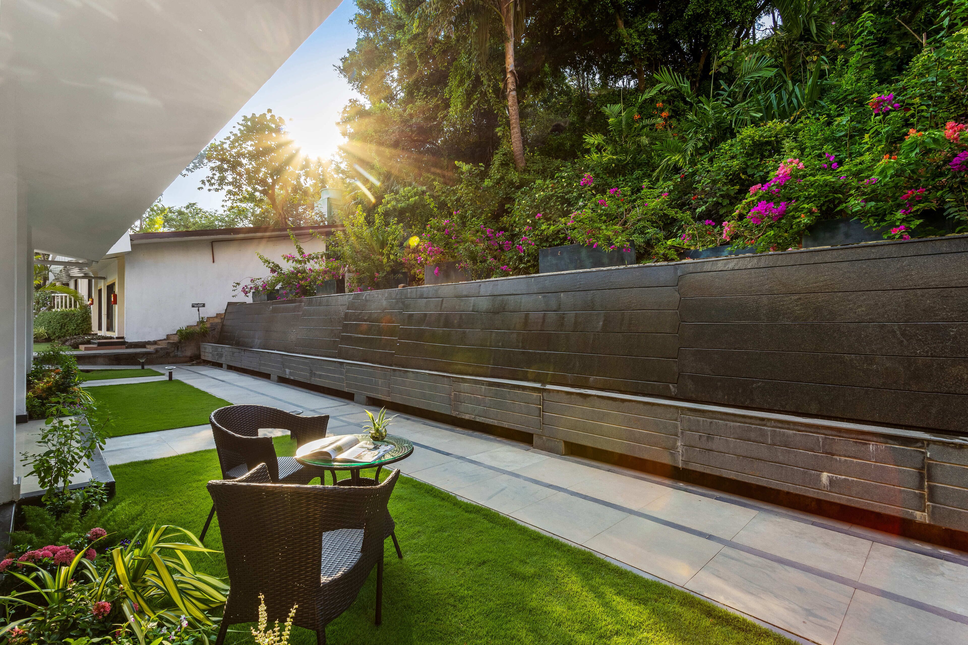 A modern outdoor patio with a dining area, a well-maintained lawn, and a stone wall with flowering plants.