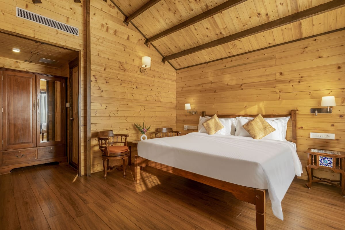 A wooden-paneled room with a large bed, a wooden wardrobe, and a small table with a chair.