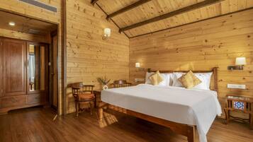 A wooden-paneled room with a large bed, a wooden wardrobe, and a small table with a chair.