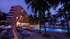 A hotel with a pool area, sun loungers, and palm trees. - Bogmallo Beach Resort (Marmagao)