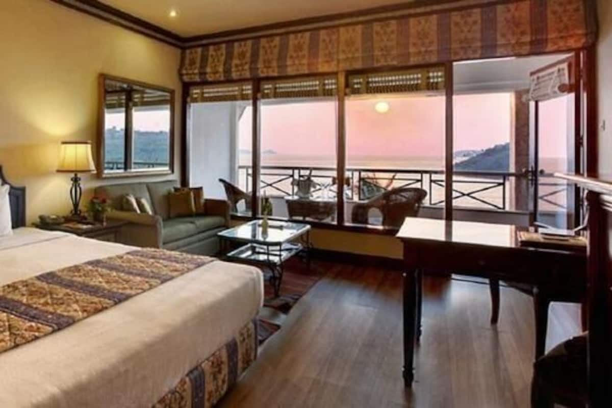 A hotel room with a large bed, a desk, a chair, and a view of the sea.