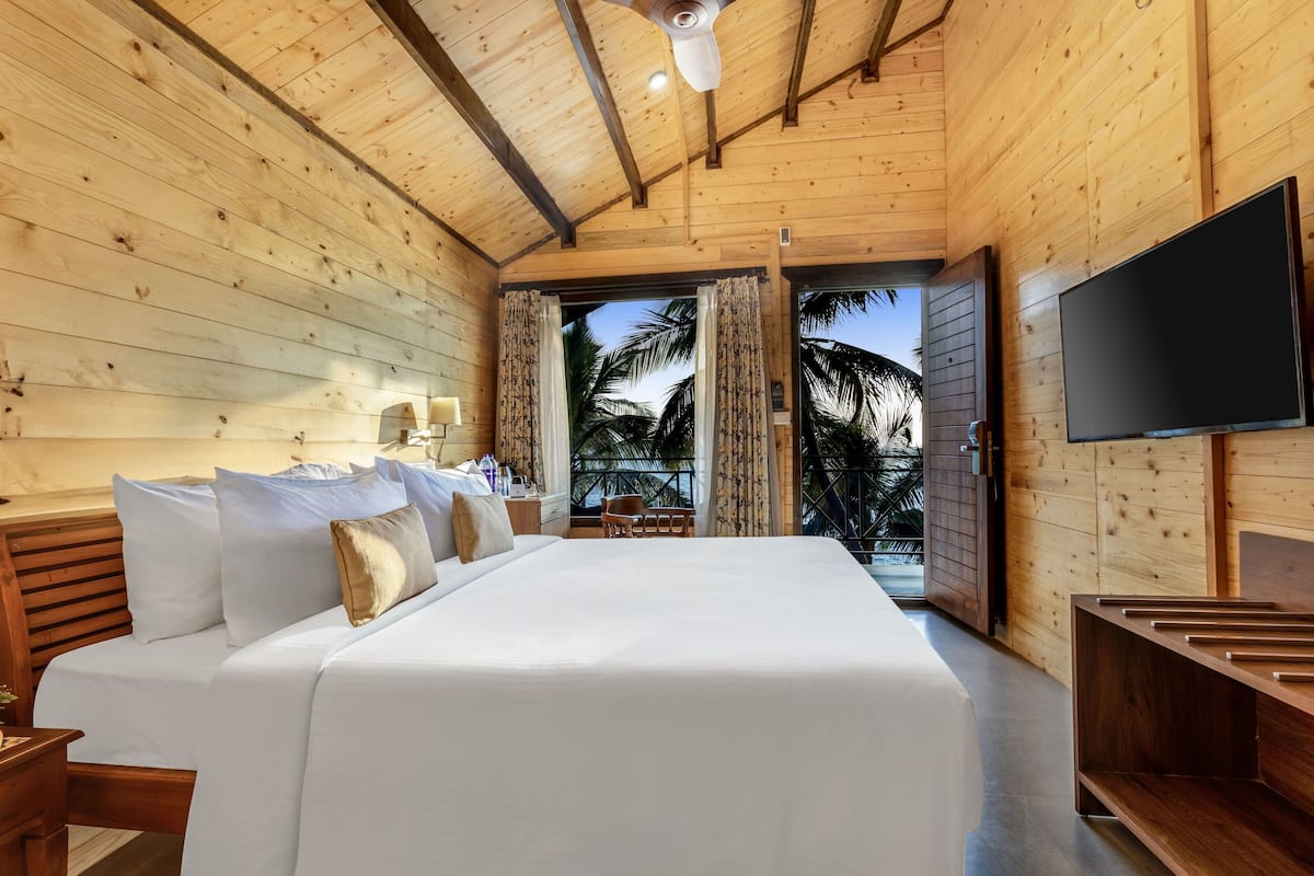 A wooden room with a bed, a TV, and a view of palm trees.