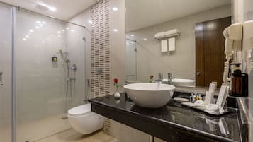 Un baño moderno con ducha de vidrio, lavamanos blanco y un espejo grande.