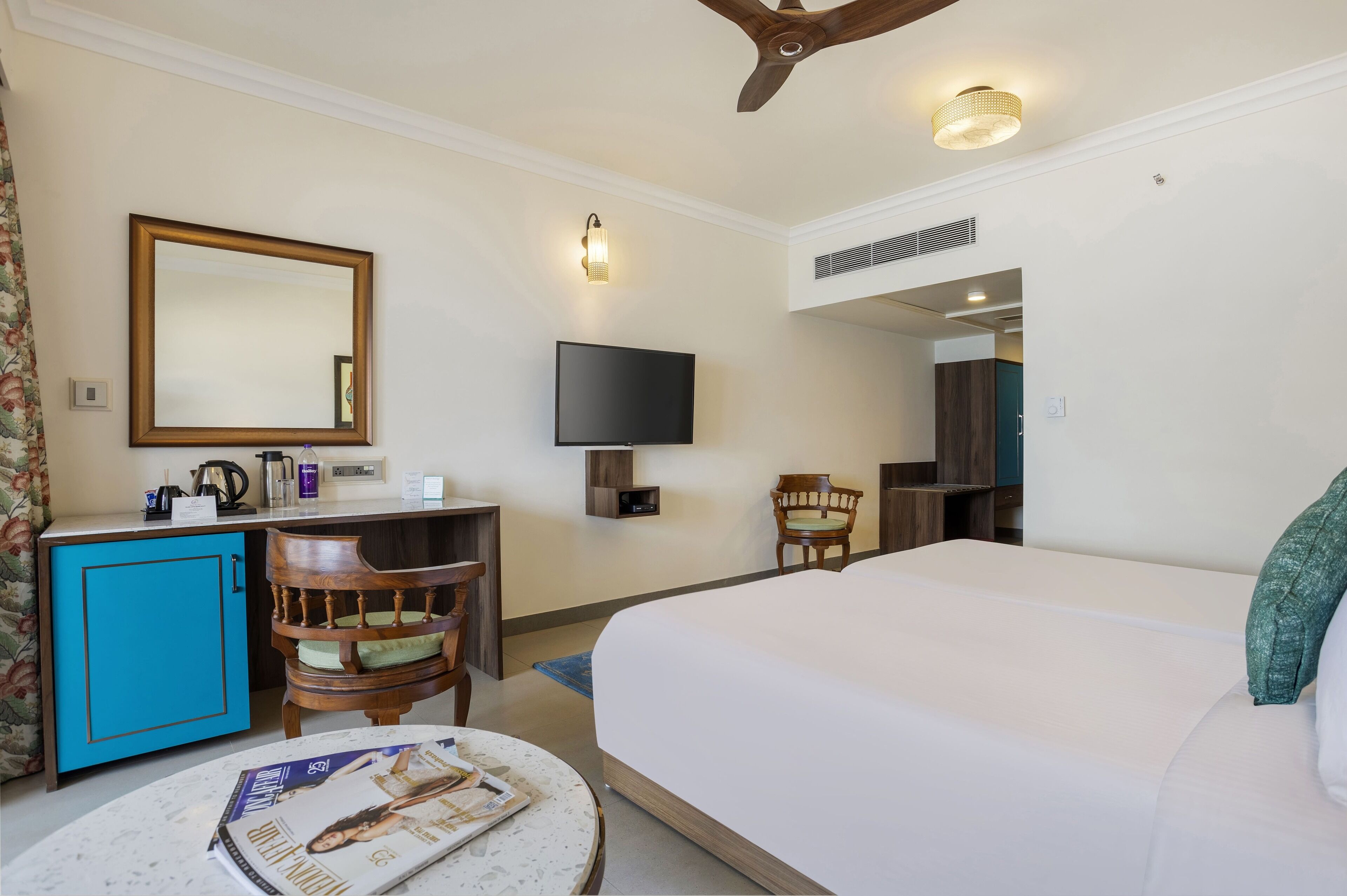 A hotel room with a bed, a desk with a chair, a television, a mirror, and a ceiling fan.