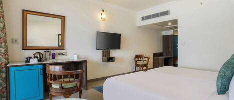 A hotel room with a bed, a desk with a chair, a television, a mirror, and a ceiling fan.