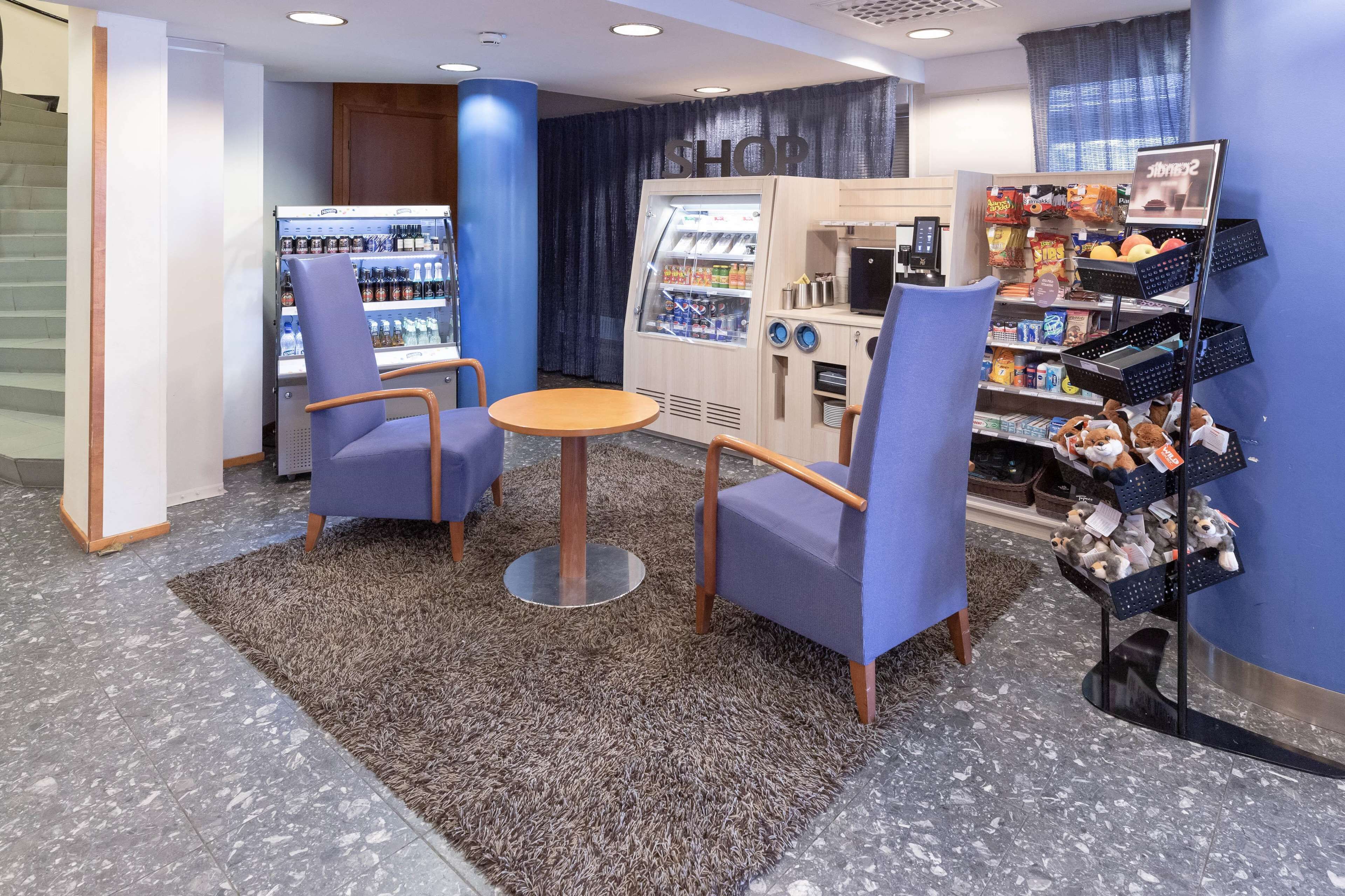 A seating area with two chairs and a small round table, a vending machine, and a shelf with plush toys.