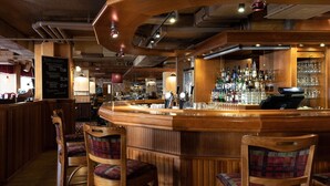 Zona de bar con taburetes de madera y una barra que exhibe diferentes botellas y vasos.
