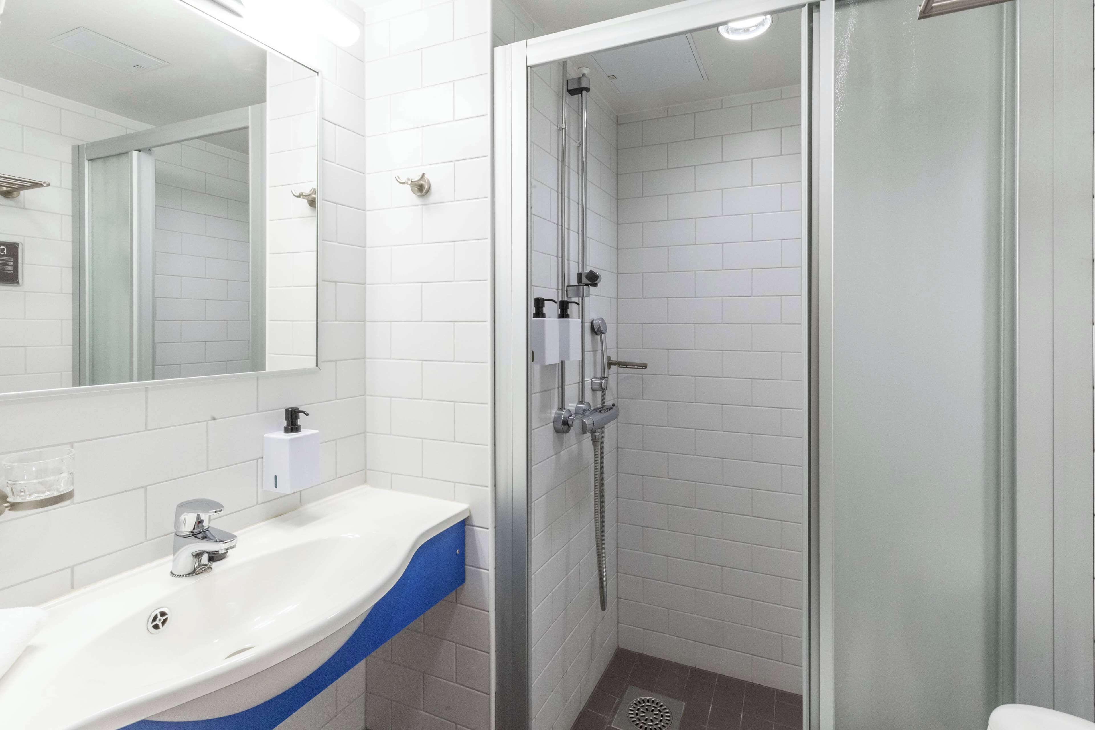 Une salle de bain avec un lavabo blanc, un miroir et une douche séparée par une paroi en verre.