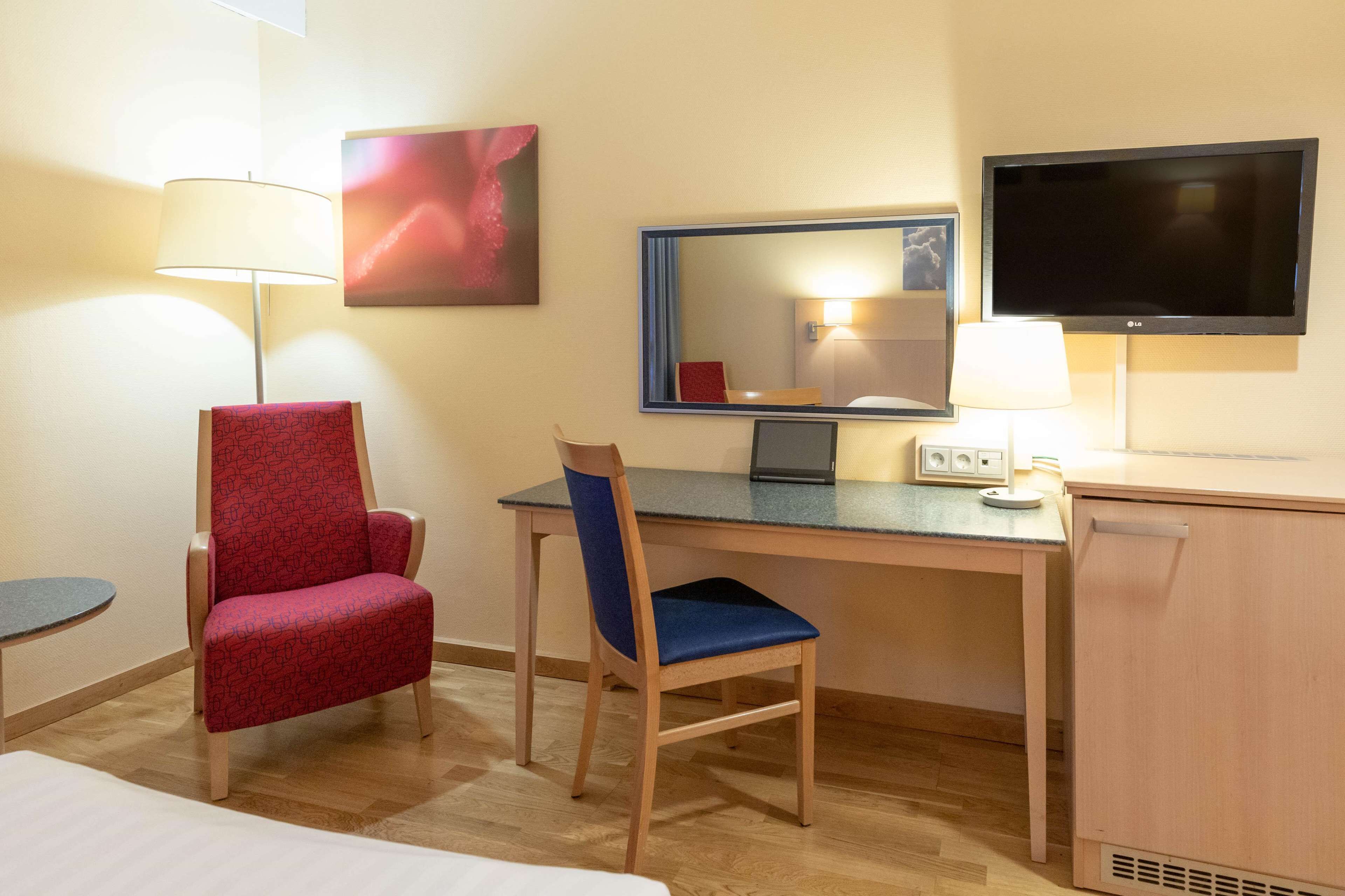 Una habitación de hotel con cama, escritorio, silla, televisión y lámpara.
