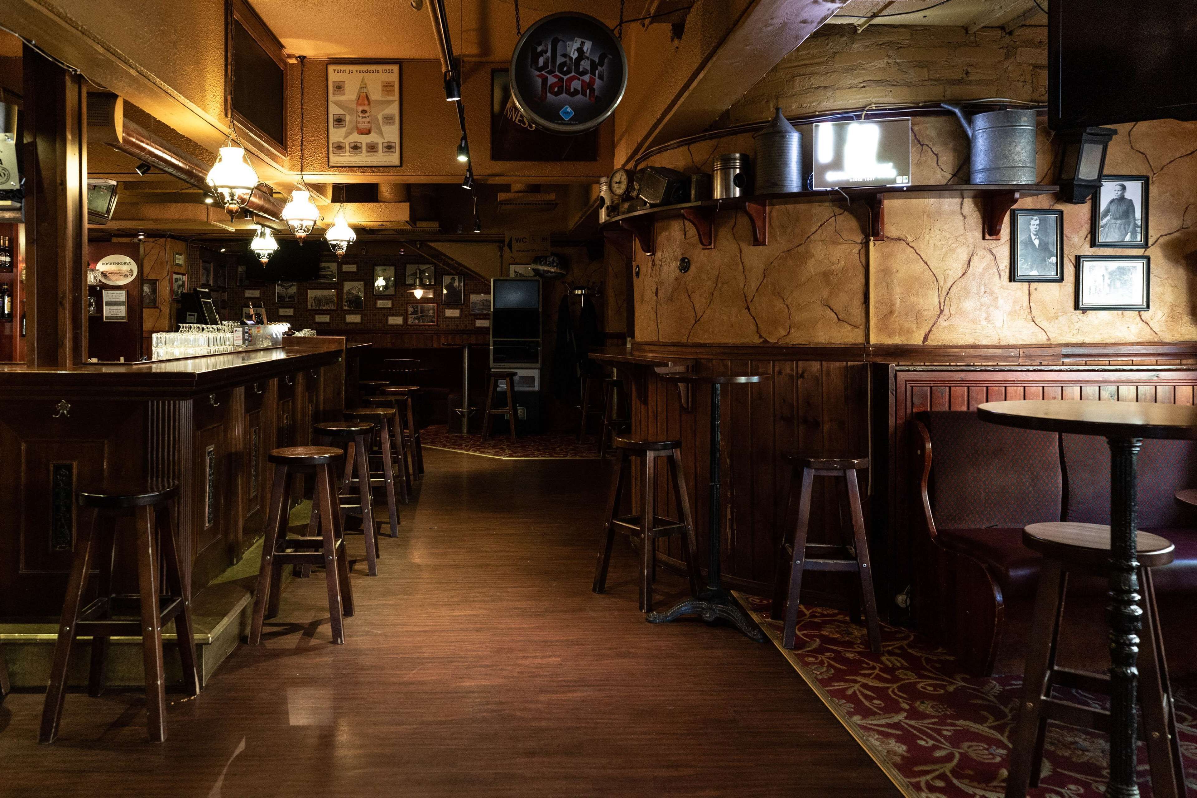A bar area with wooden stools, a bar counter, and a vintage decor including a clock and framed pictures on the wall.
