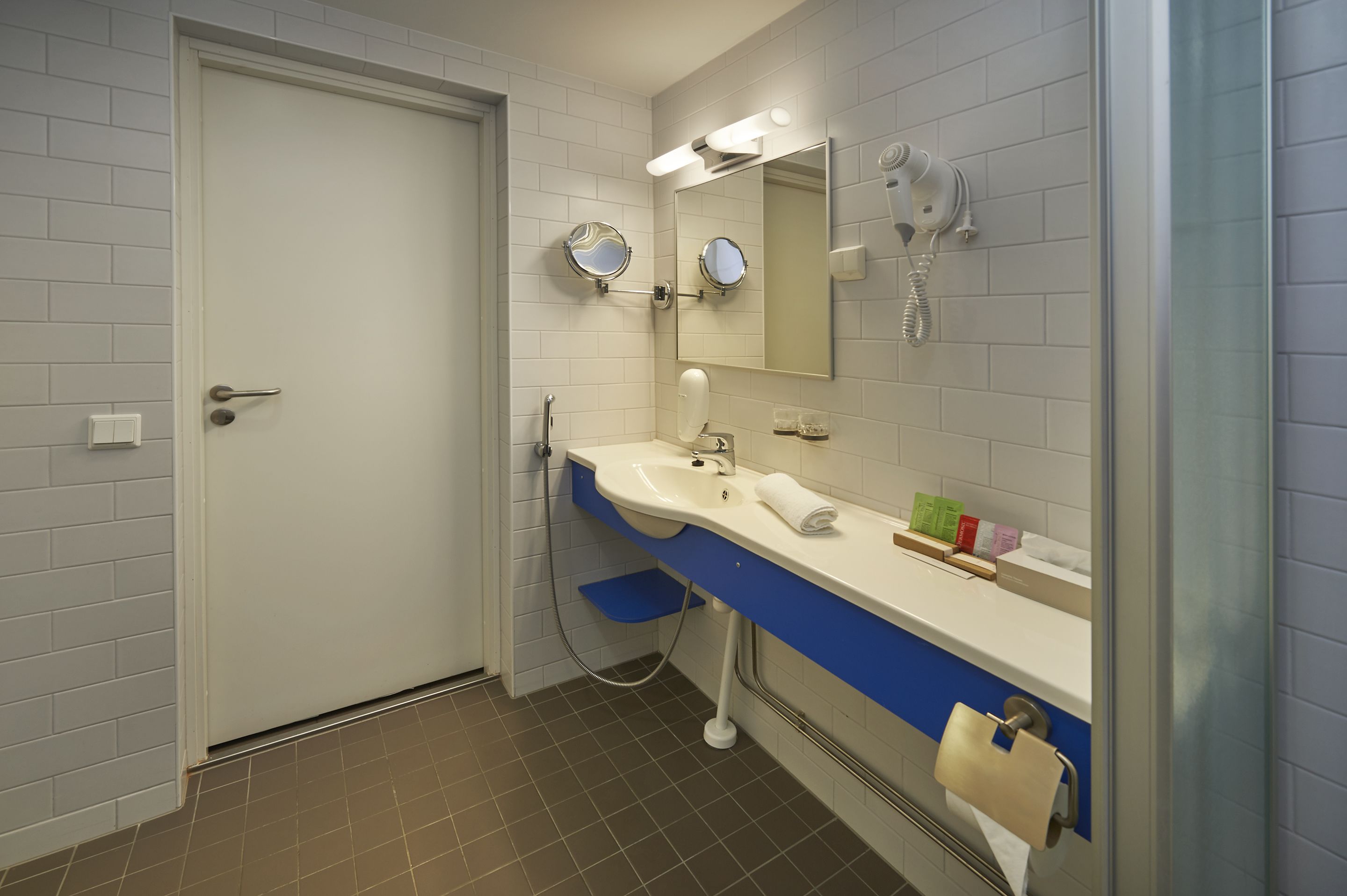 A bathroom with a white door, a sink with a blue countertop, a mirror, a hairdryer, and a towel rack.