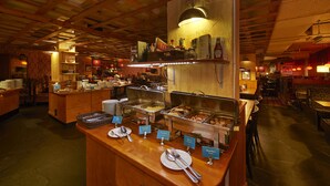 Un área de bufé con varias estaciones de comida, mostradores de madera y un techo alto con vigas a la vista.