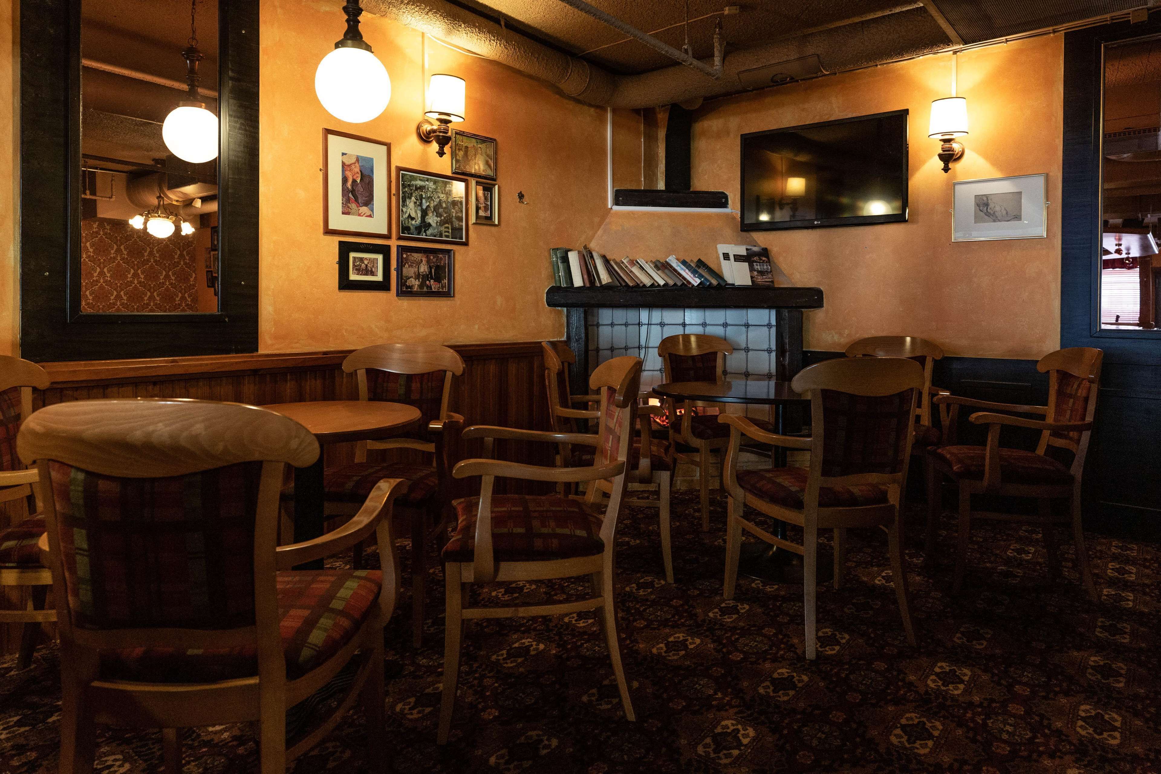 A cozy room with wooden chairs and tables, a fireplace, and wall-mounted lamps.