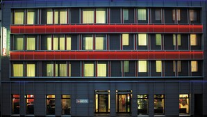 Un hotel de varios pisos con una fachada moderna, que presenta un llamativo detalle rojo en el nivel superior.