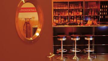 Eine Bar mit Spiegelwand, Regalen voller Flaschen und drei Barhocker.