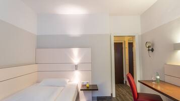 A modern hotel room with a bed, bedside table, and a desk with a chair.