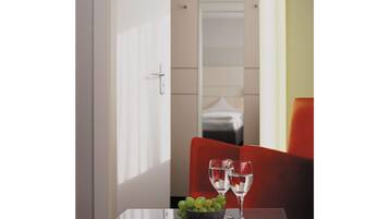 A glass table with a bowl of grapes and two glasses of water, a red chair, and a white door in the background.