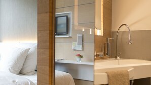 Ett modernt hotellrum med en säng, ett badrum med handfat och en spegel.