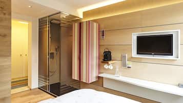 Ein modernes Hotelzimmer mit Dusche, Fernseher, Nachttisch und Bett.