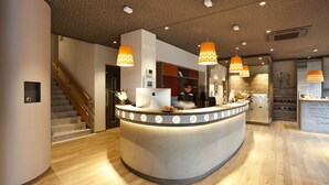 Ett receptionsområde med en böjd receptionsdisk, en trätrappa och hängande lampor.