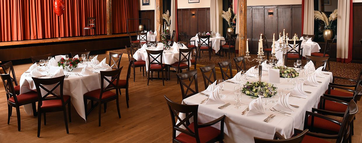 A formal dining area with round tables set for multiple guests, featuring white tablecloths and red upholstered chairs.