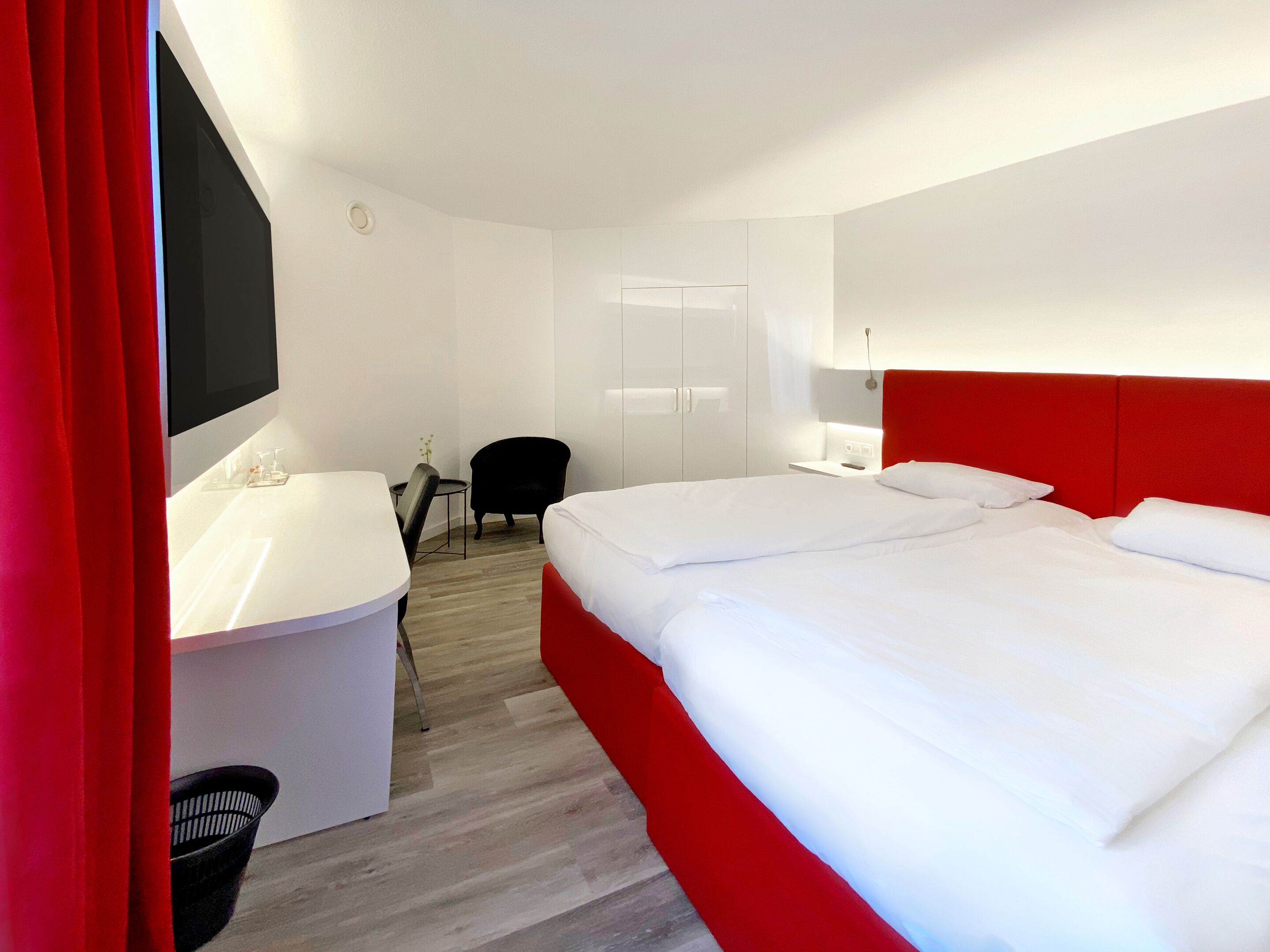 Quarto de hotel com cama, escrivaninha, cadeira, banheiro e televisão.