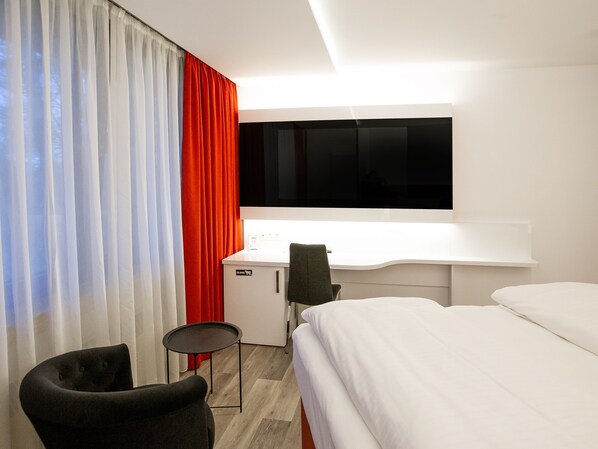 A hotel room with a bed, a desk, a chair, and a window with curtains.