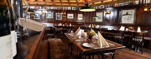 A restaurant with wooden tables, chairs, and a bar area with a bottle of wine.