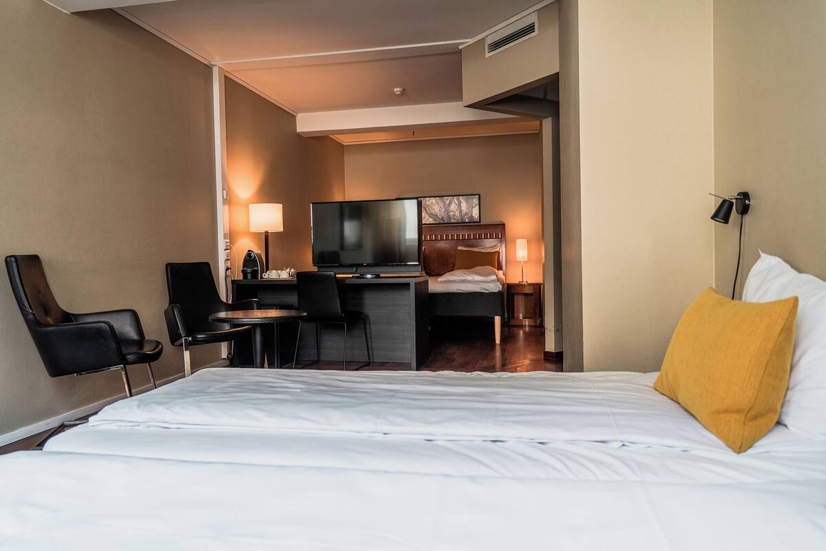A hotel room with a bed, a desk, a chair, a television, and a lamp.