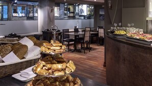 Een buffetgedeelte met diverse gebakjes en belegde broodjes, een zithoek met tafels en stoelen, en een balie met fruit en andere etenswaren.
