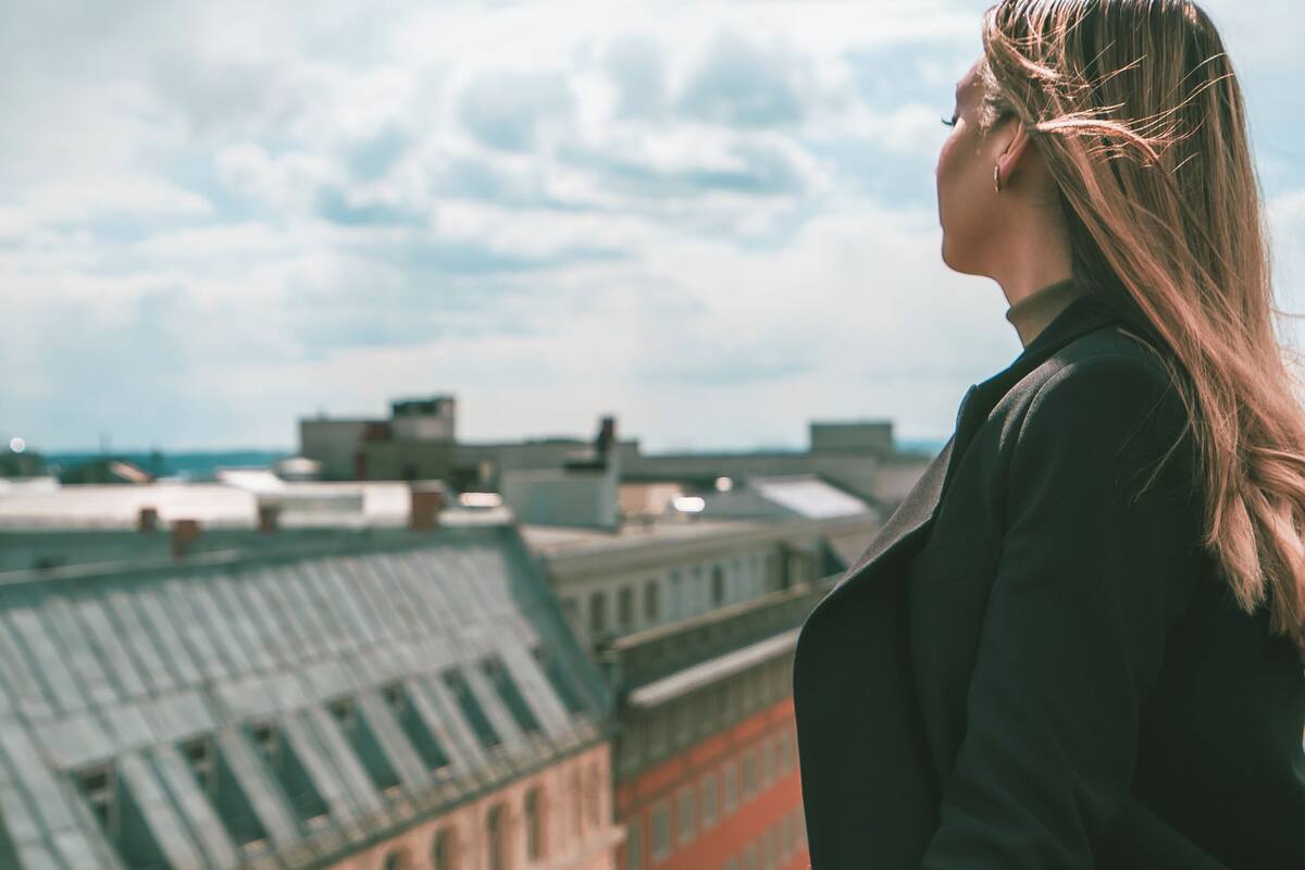 A person standing on a balcony overlooking a cityscape with buildings and a clear sky.