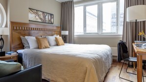 Een hotelkamer met een groot bed, een bureau met stoel, een lamp en een raam met gordijnen.