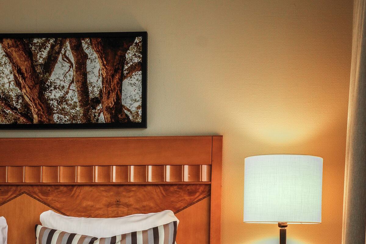 A neatly made bed with striped pillows, a wooden headboard, and a bedside table with a lamp.