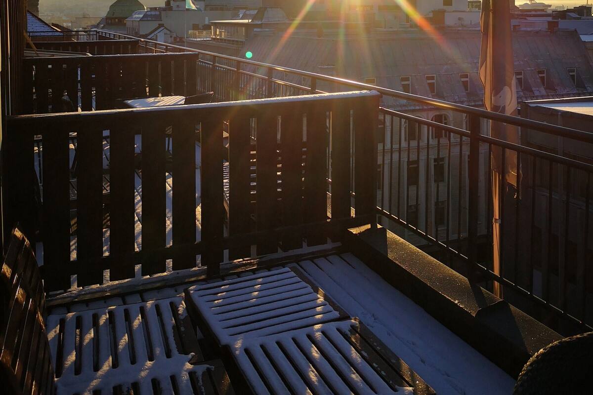 A rooftop with a view of a cityscape, including a church spire, during sunset.