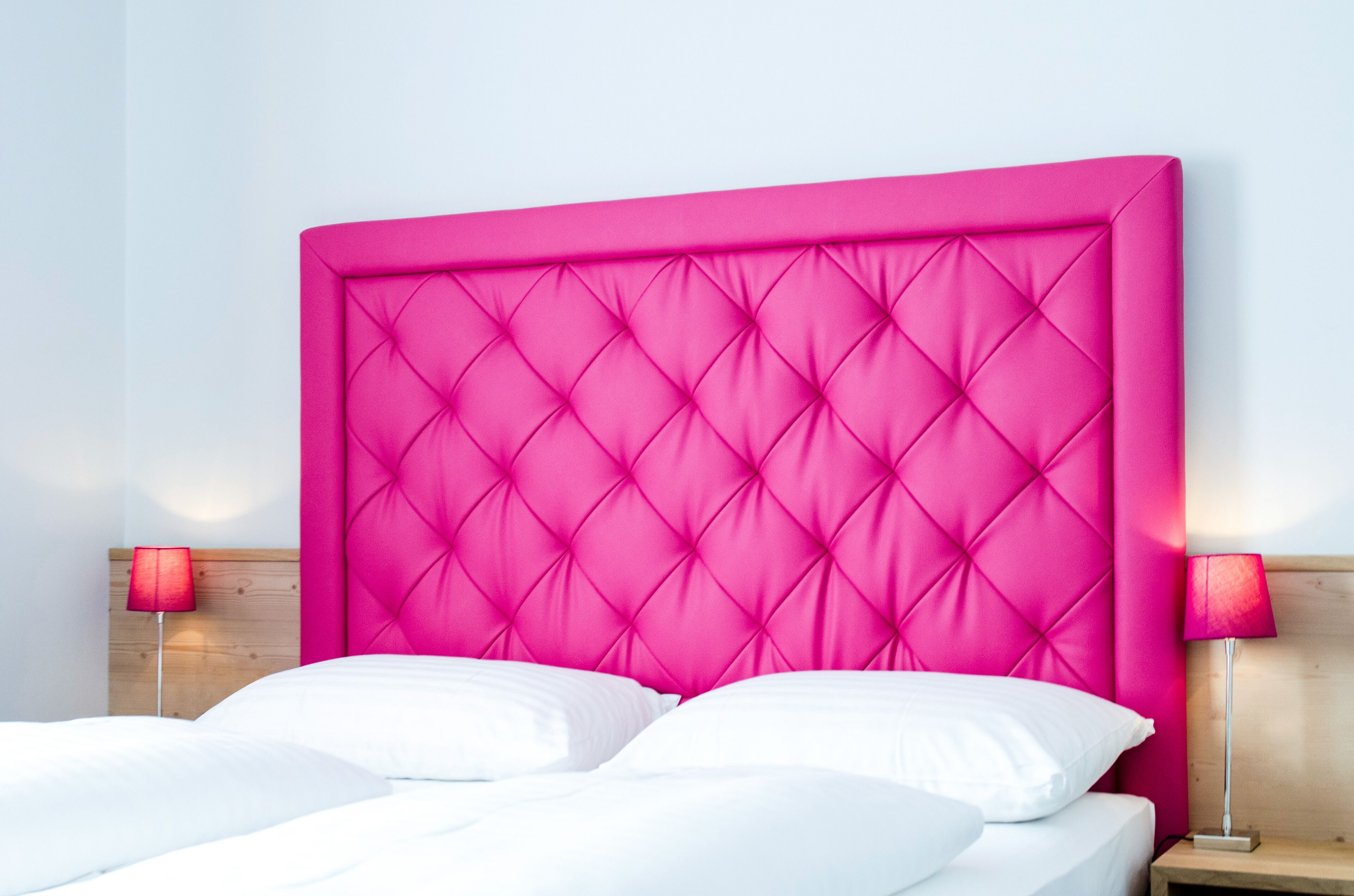 Ein Bett mit einem gepolsterten, rosa Kopfende, weißen Kissen und zwei Nachttischlampen.