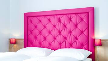 Ein Bett mit einem gepolsterten, rosa Kopfende, weißen Kissen und zwei Nachttischlampen.