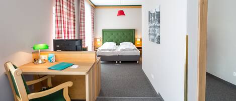Una habitación pequeña y bien iluminada con una cama, un escritorio con una silla, un televisor y una lámpara colgante roja.