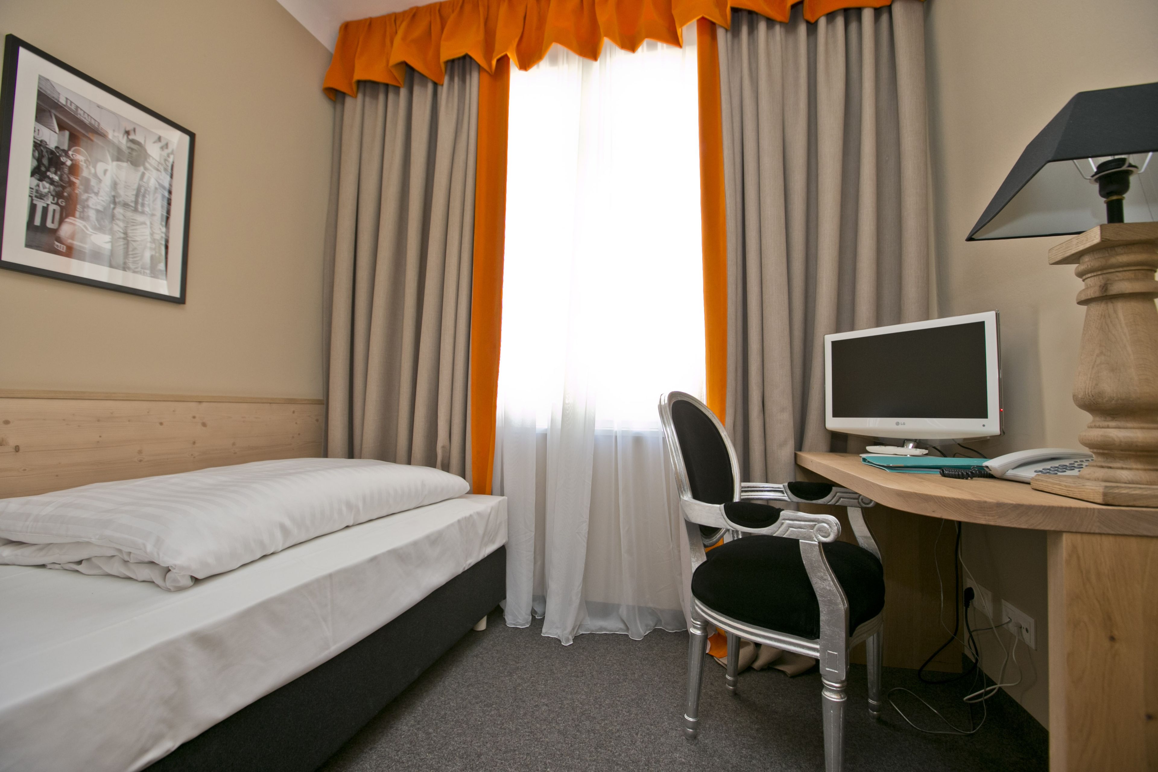 A hotel room with a bed, a desk with a computer, a chair, and a lamp.