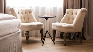 Una habitación con dos sillones tapizados, una mesita redonda y una cama.