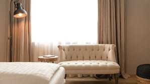 Un dormitorio con una cama, un sillón capitoné, una mesita redonda y una lámpara de pared.