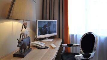 A hotel room with a desk, a lamp, a television, a telephone, and a chair.