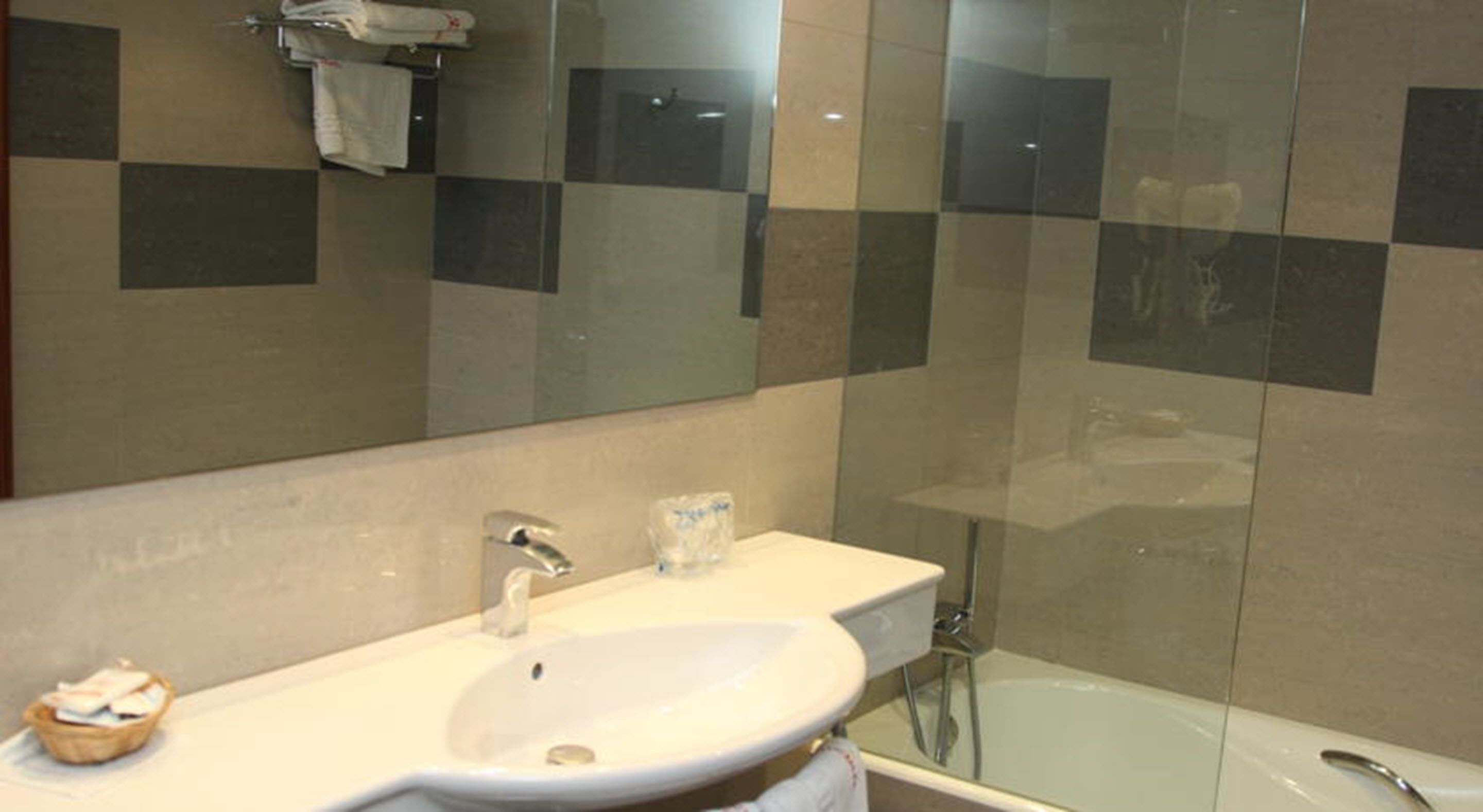 Un baño con lavamanos blanco, espejo y ducha con mampara de vidrio.