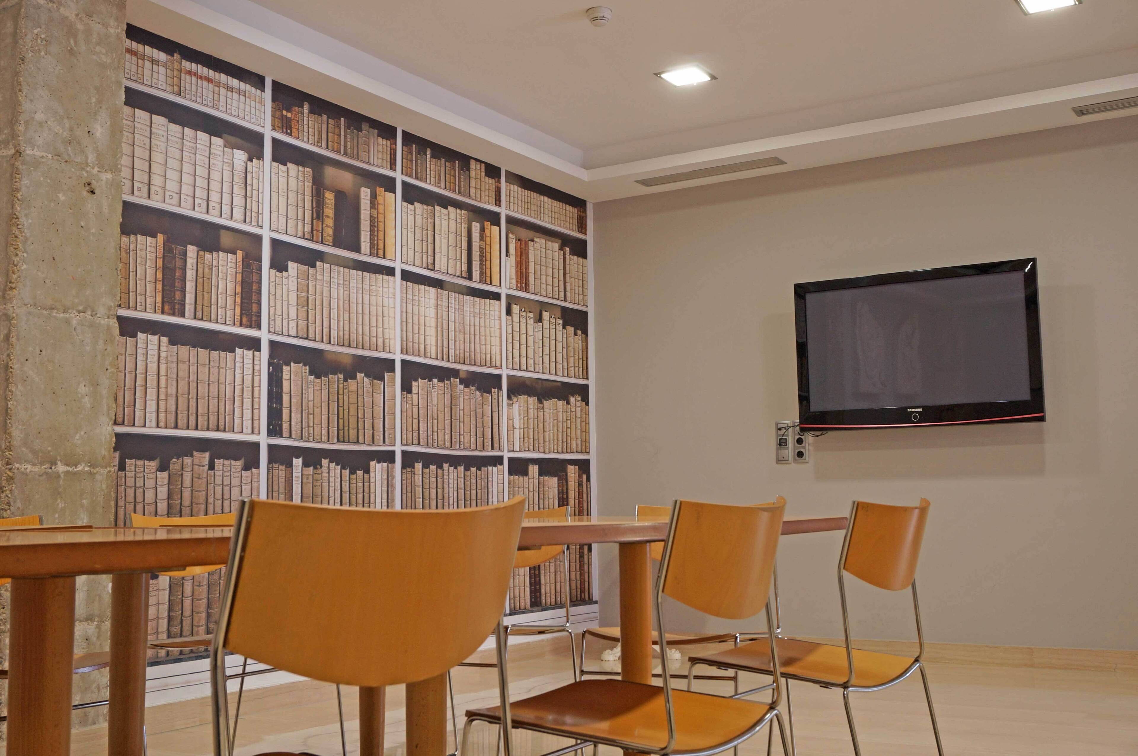 Una biblioteca con estanterías, un televisor y sillas de madera.