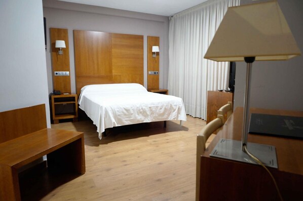 Une chambre d’hôtel avec un lit simple, une tête de lit en bois, un bureau, une chaise, une lampe et une table de chevet.