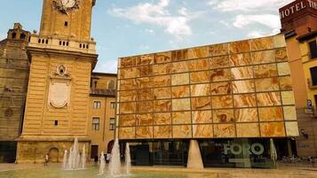 Un edificio histórico con una torre de reloj, una fuente y una fachada moderna de vidrio.