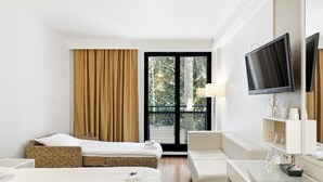 Een hotelkamer met twee bedden, een bank, een televisie en een raam met uitzicht op bomen.
